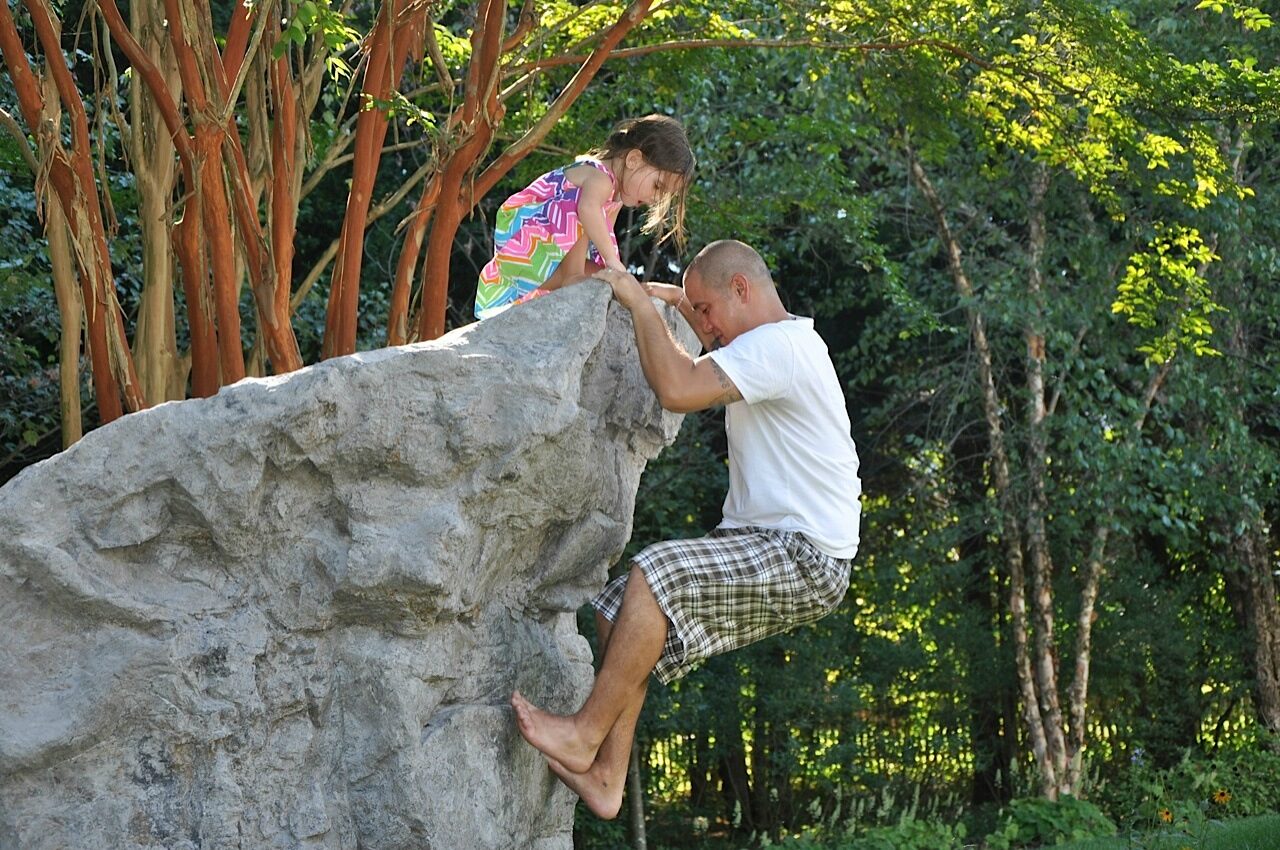 Father and daughter climbing boulder